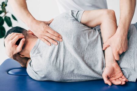 Back view of chiropractor massaging back of man lying on Massage Table in hospitalの写真素材