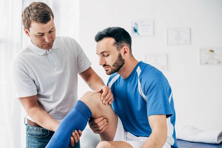 Physiotherapist massaging leg of handsome football player in hospitalの写真素材