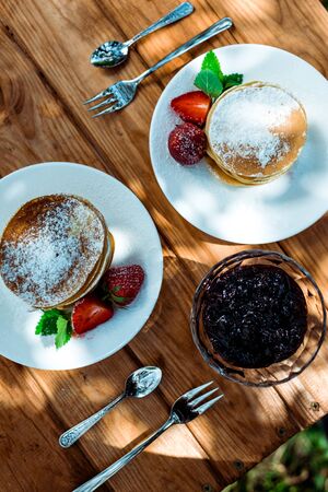 Top view of tasty and sweet pancakes with fresh strawberries and jam in bowl