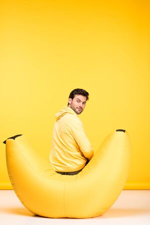 Man sitting on bean bag chair on yellow background and looking at cameraの写真素材
