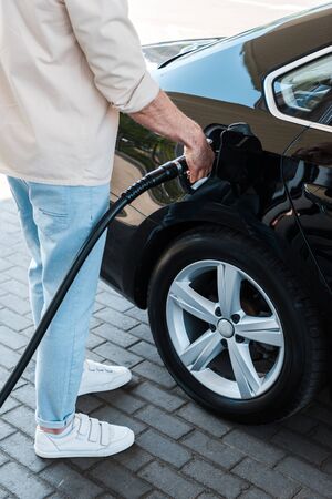 Cropped view of man holding fuel nozzle and refueling automobile at gas station