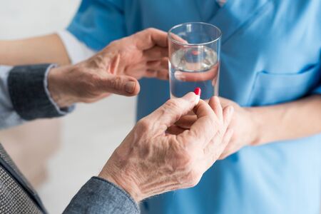 Cropped view of elderly man holding pills in hand, while doctor giving glass with water to patientの写真素材