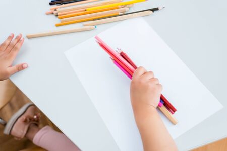Cropped view of kid holding colorful pencils near paperの写真素材