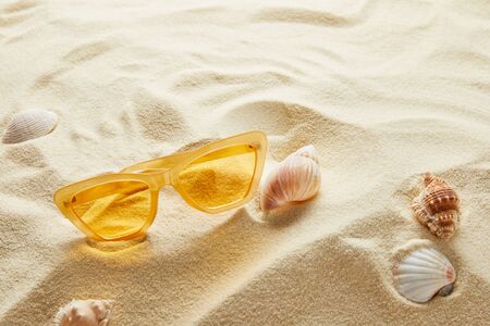 Yellow stylish sunglasses on sand with seashellsの写真素材