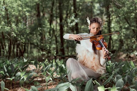 Beautiful woman in white swan costume playing on violinの写真素材