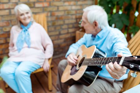 Selective focus of retired husband playing acoustic guitar near wifeの写真素材