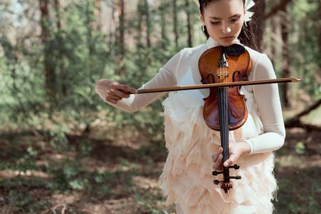 Young woman in white swan costume standing on forest background with violinの写真素材