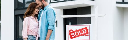 Panoramic shot of happy man and woman with closed eyes standing near house