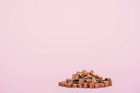 Pile of brown sugar cubes on pink background with copy space