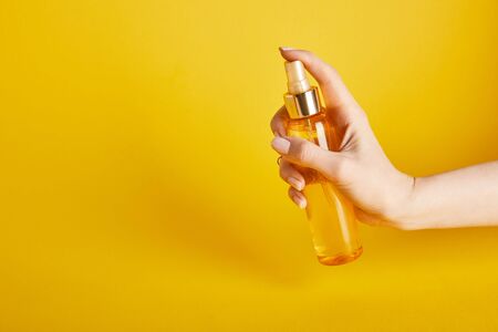 Cropped view of woman holding suntan oil in spray bottle on yellow backgroundの写真素材