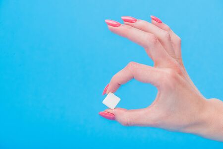 Cropped view of woman holding white sugar cube isolated on blue backgroundの写真素材
