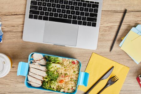 Top view of workplace with laptop and lunch box with tasty risotto and chicken on wooden table, illustrative editorialの写真素材