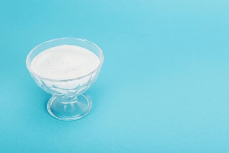 Glass bowl with white granulated sugar on blue background with copy spaceの写真素材