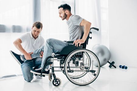 Physiotherapist massaging leg of handicapped man in wheelchairの写真素材