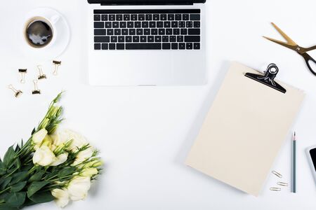 Top view of laptop, cup of coffee, clipboard, flowers, scissors, pencil, binder clips and paper clips of white backgroundの写真素材