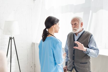 Senior man standing inside home with copy space, and talking with nurse