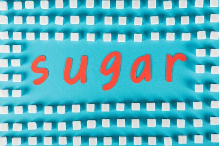 Top view of red paper cut word sugar surrounded by white sugar cubes on blue surface backgroundの写真素材