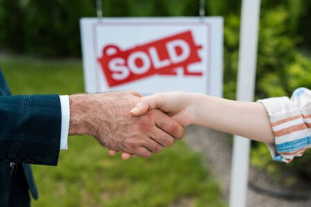Cropped view of broker and woman shaking hands near board with sold lettersの写真素材