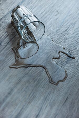 Glass with spilled water on textured wooden surfaceの写真素材