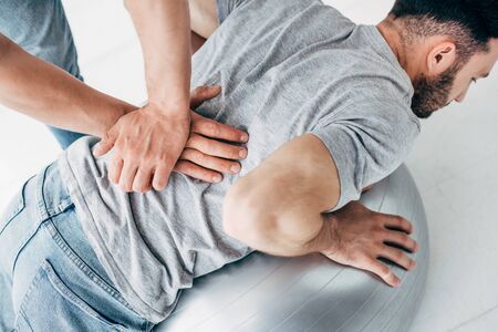 Chiropractor massaging back of man lying on fitness ballの写真素材