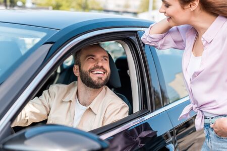 Selective focus of happy woman standing with hand in pocket near cheerful man in carの写真素材