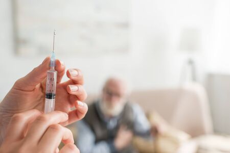 Selective focus of woman hands with syringe on senior man backgroundの写真素材