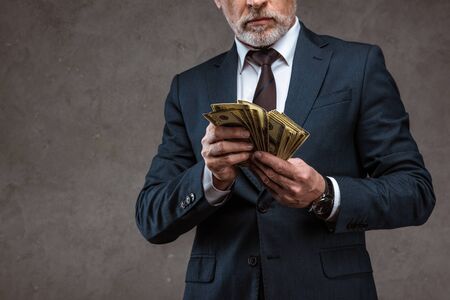 Cropped view of businessman in suit holding dollar banknotes in hands on grey background