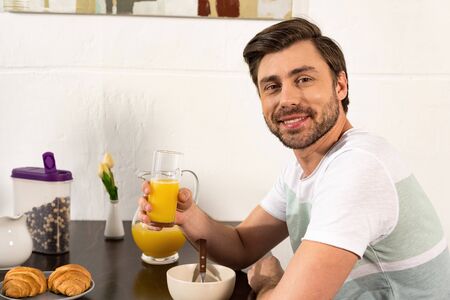 Smiling bearded man holding glass of orange juice during breakfast