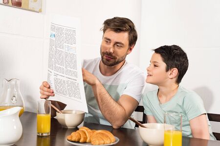 Dad and son reading newspaper during breakfast in kitchenの写真素材