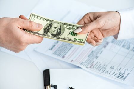 Cropped view of man and woman holding dollar banknotes near clipboard and documents