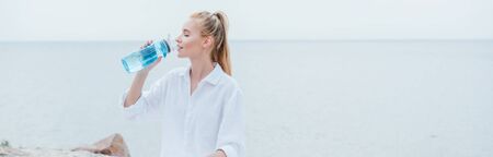 Panoramic shot of happy blonde woman drinking water