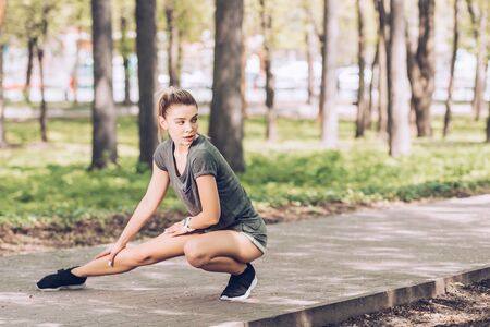 Attractive young woman in sportswear looking away while exercising in sunny parkの写真素材