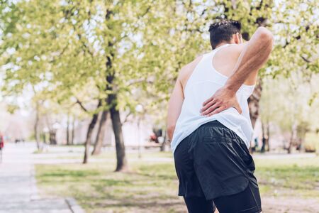 Back view of sportsman suffering from pain while touching injured backの写真素材