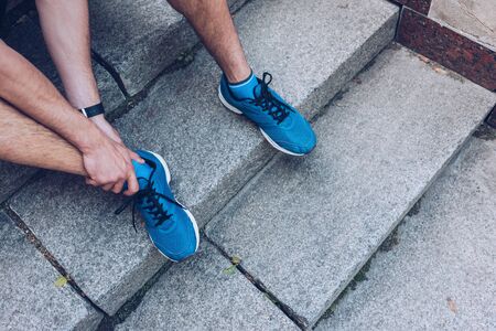Cropped shot of man in sneakers sitting on stairs and touching injured leg