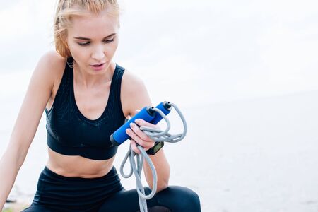 Attractive and tired young woman in sportswear looking at jump rope