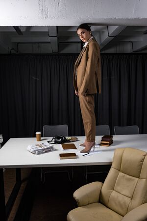 Side view of fashionable businesswoman standing on table in office, looking at cameraの写真素材