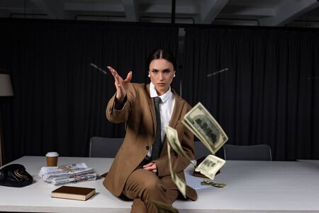 Businesswoman sitting on table, throwing money and looking at camera
