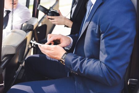 Cropped view of businessman in formal wear sitting in helicopter with smartphoneの写真素材