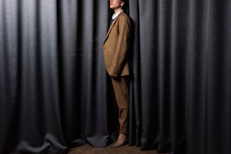 Side view of fashionable model in suit standing in studio with grey curtain backgroundの写真素材