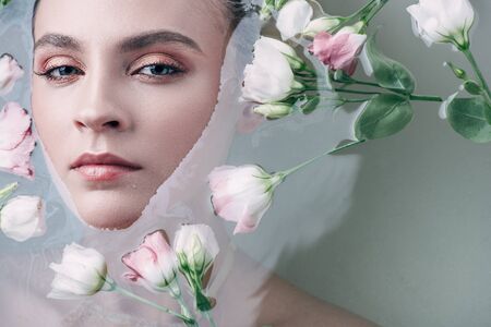Top view of beautiful woman lying in clear water with flowers and looking at camera