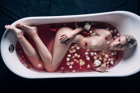 Top view of sexy woman in beige lingerie in bathtub with pink water and petalsの写真素材