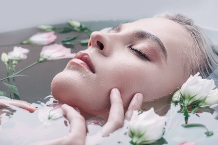 Beautiful woman with closed eyes lying in clear water with flowers