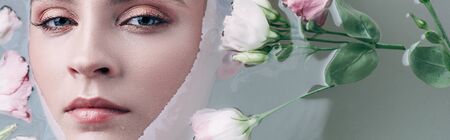 Top view of beautiful woman lying in clear water with flowers in white bathtub and looking at cameraの写真素材