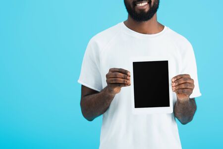 Cropped view of African American man in white t-shirt showing digital tablet with blank screen isolated on blue backgroundの写真素材