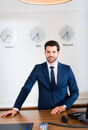 Cheerful bearded receptionist standing at reception desk in hotelの写真素材