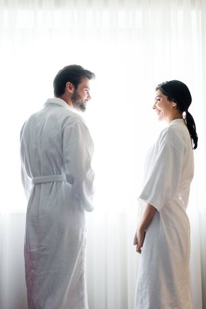 Low angle view of happy man and attractive woman in bathrobes standing and looking at each otherの写真素材