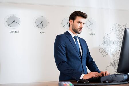 Low angle view of confident receptionist in suit looking at computer monitor in hotelの写真素材