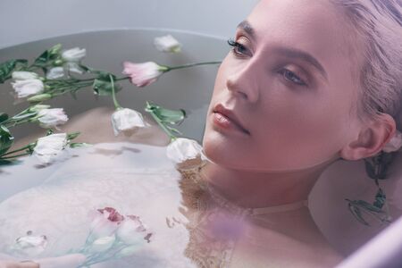 Beautiful woman in lace underwear lying in water with flowers in white bathtub