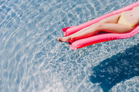 Cropped view of sexy slim woman in swimsuit swimming on pink pool float in swimming pool