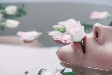 Partial view of beautiful woman lying in clear water with rose in mouth
